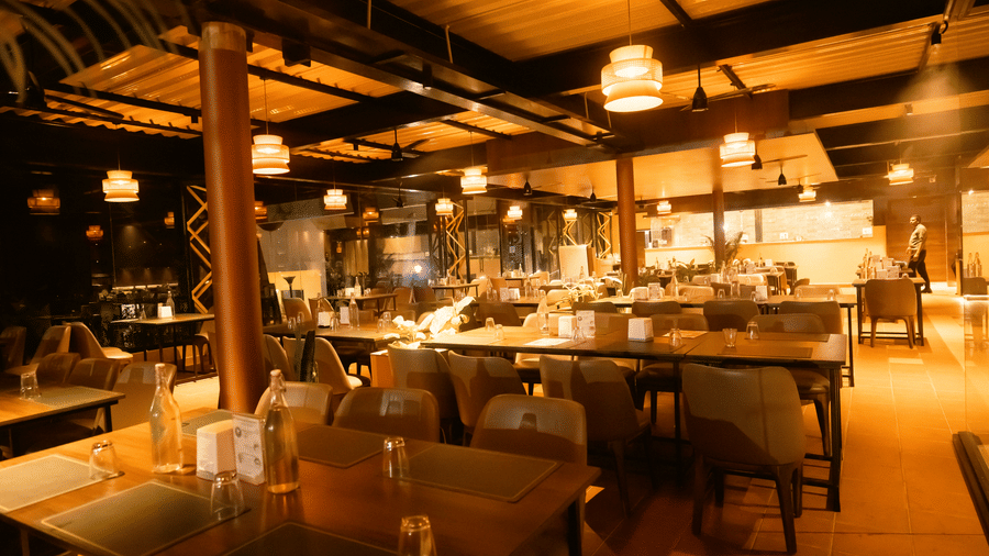 Interior view of the DNC Shevaroys Resort & Spa restaurant showing wooden pillars, hanging lamps, and a mix of dining furniture.