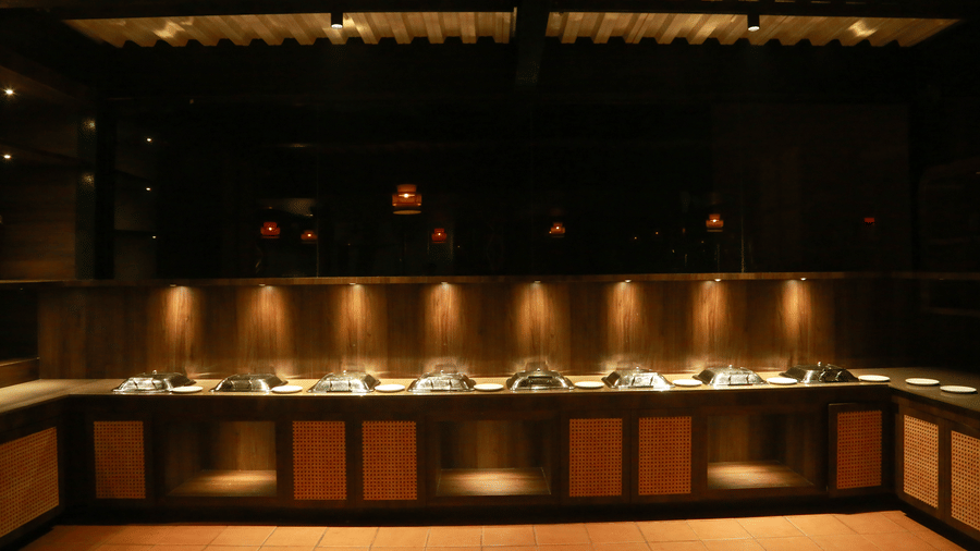 A lit buffet counter at DNC Shevaroys Resort & Spa with overhead spotlights illuminating the food service area at night.