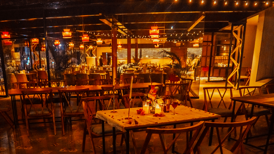 An evening view of the restaurant at DNC Shevaroys Resort & Spa with warm decorative lighting and tables prepared for dinner.