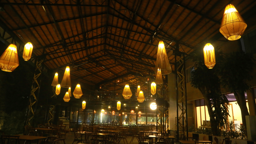 An open-sided dining area at DNC Shevaroys Resort & Spa illuminated by numerous hanging woven lanterns under a dark pitched roof.