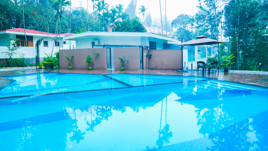 An outdoor swimming pool with clear water surrounded by greenery and resort building at DNC Shevaroys Resort & Spa.
