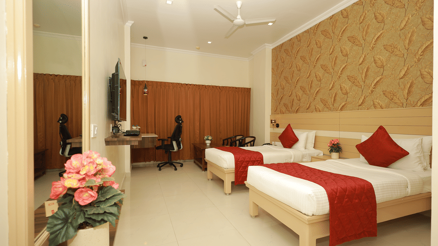 An Executive Room at DSF Grand Plaza, Tuticorin with 2 twin beds dressed in red throws, a leaf-patterned feature wall, a wall-mounted TV, and a mirrored wardrobe.