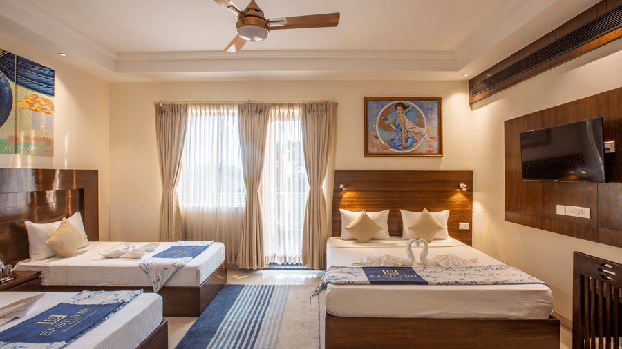 A spacious family-style room with 3 separate beds, blue striped rugs, and large windows for natural light — Eastlynn Resort, Rishikesh