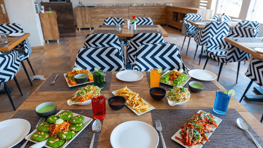 Dining table with patterned chairs, plates, drinks, and a spread of dishes, at Ewaka Ganga, Rishikesh.