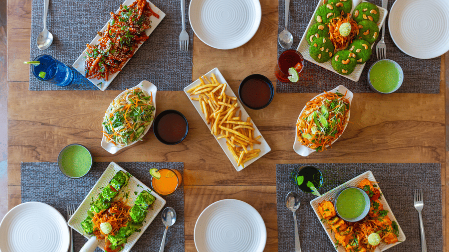 Dining table with plates, glasses, and multiple dishes served on rectangular plates, at Ewaka Ganga, Rishikesh.