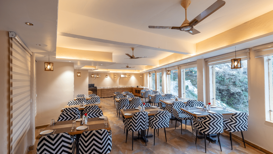 Wide dining space with multiple tables, chairs, and ceiling lights, at Ewaka Ganga, Rishikesh.