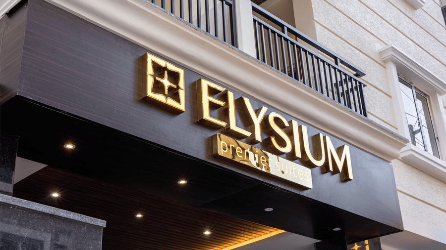 A close-up of the elegant gold ELYSIUM signage mounted on a dark brown textured beam above the hotel entrance.