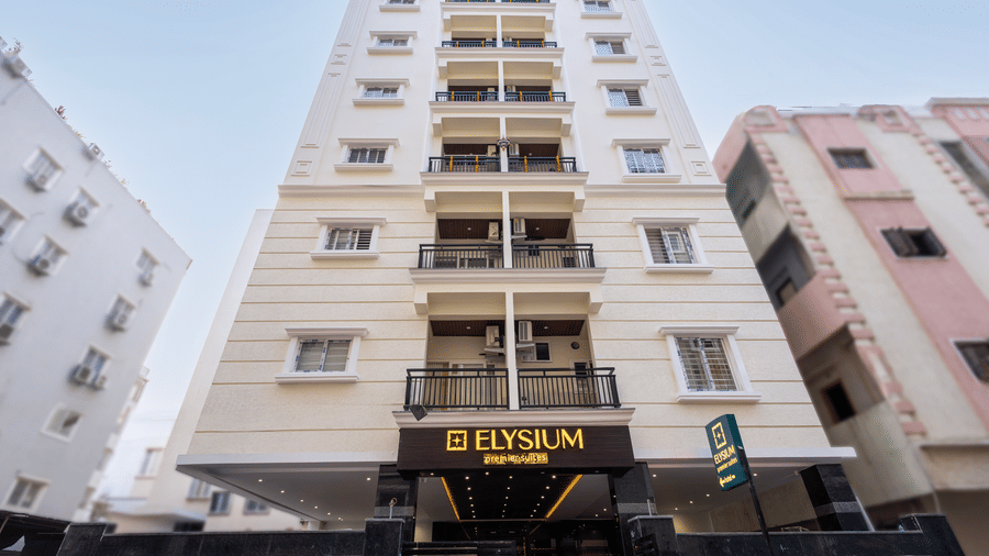 A full vertical view of the tall hotel exterior, highlighting the neat rows of windows and balconies against a bright afternoon sky at ELYSIUM Premier Suites, HITEC City.