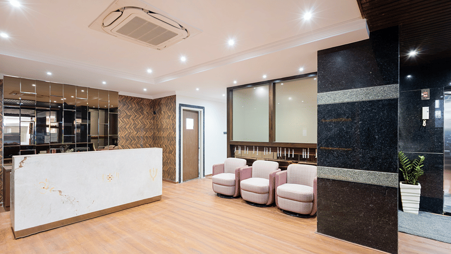 A sleek bathroom interior with a minimalist vanity unit, a wall-mounted mirror, and polished chrome fixtures against neutral tiling at ELYSIUM Premier Suites, HITEC City.