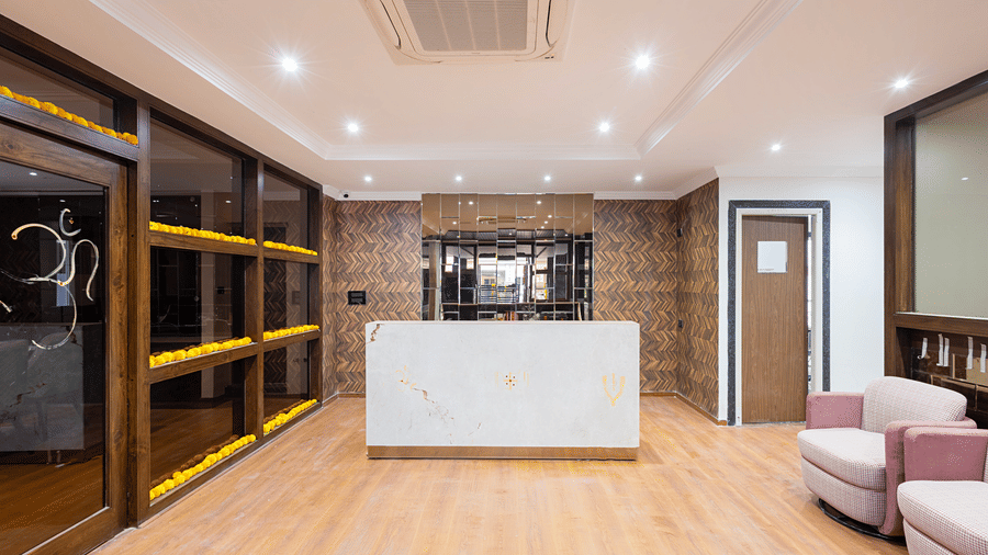 A clean, modern hotel bathroom featuring a large walk-in shower with a glass screen, a white basin, and large-format grey tiles at ELYSIUM Premier Suites, HITEC City.