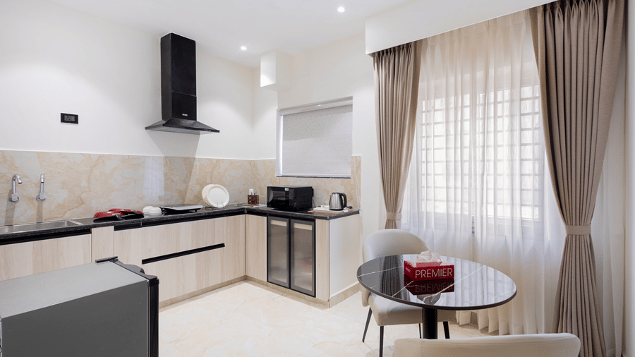 A contemporary kitchenette and dining nook with a small round table, sleek light-wood cabinetry, and a black extractor hood at ELYSIUM Premier Suites, HITEC City.