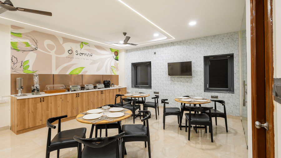 A dining area with tables and chairs at Elysium Studio Suites, Madhapur, has wall decorations and overhead lights.