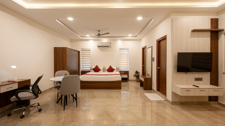 A panoramic view of a room at Elysium Studio Suites, Madhapur, shows a bed, desk, and chair on the left and right.