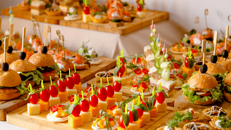 Assorted gourmet appetizers and mini burgers arranged beautifully on a wooden platter at a buffet setup.
