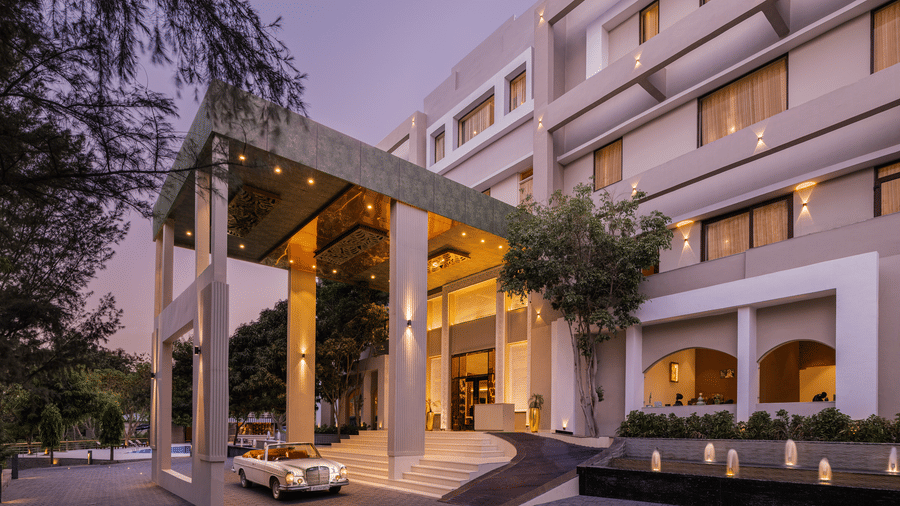 Facade of Essentia Luxury Resort & Spa, the best place in Udaipur for couples, with a car parked in the porch, trees on the left hand side and the twilight sky above.