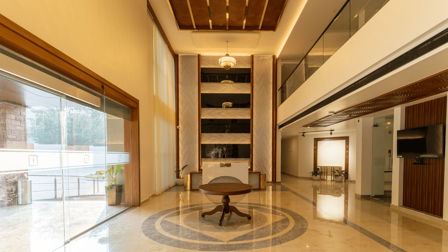 A spacious, luxurious hotel reception featuring high ceilings, marble floors with a circular inlay design, a central round table at  Essentia Resort & Spa, Sirsi 