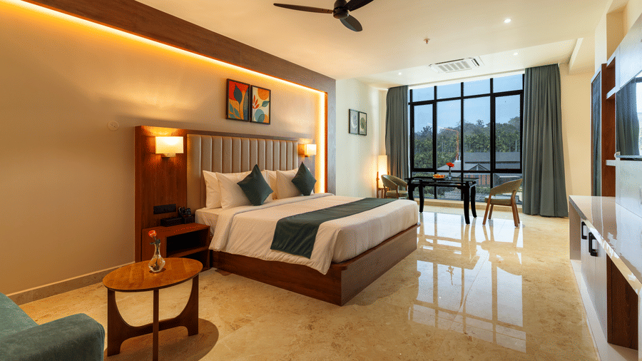 room featuring a large bed with linens and a throw blanket, the room has light-colored marble flooring, wooden accents on the wall behind the bed, and a ceiling fan, there are large windows offering a view, a small round wooden table with two chairs, and a