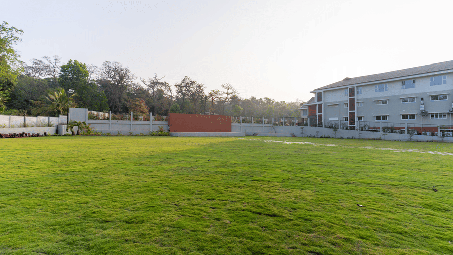 An outdoor lawn with trees in the background and a large building on the right at Essentia Resort & Spa, Sirsi  