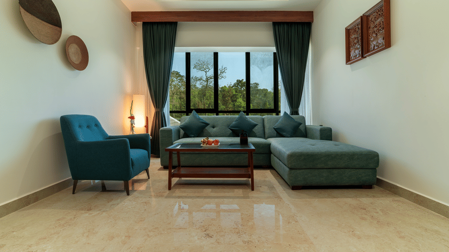 living room featuring a sectional sofa, a accent chair, a wooden coffee table, and a large window with dark curtains at  Essentia Resort & Spa, Sirsi 