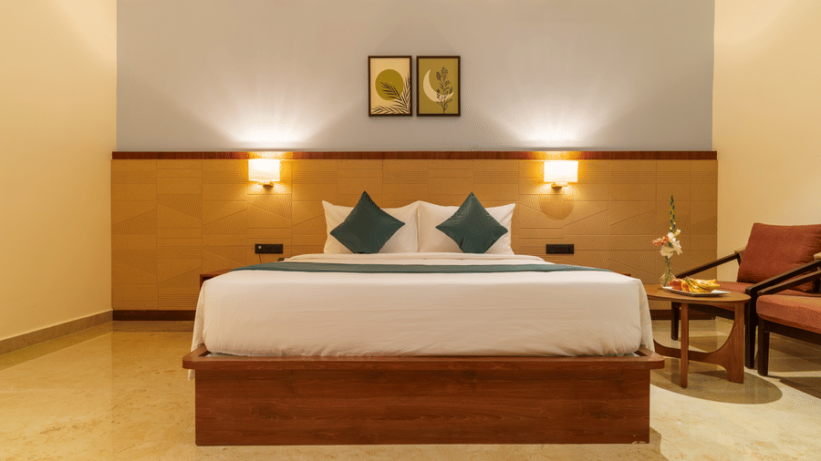 bedroom with a large bed, two pillows, two lamps, and artwork on the wall at Essentia Resort & Spa, Sirsi  