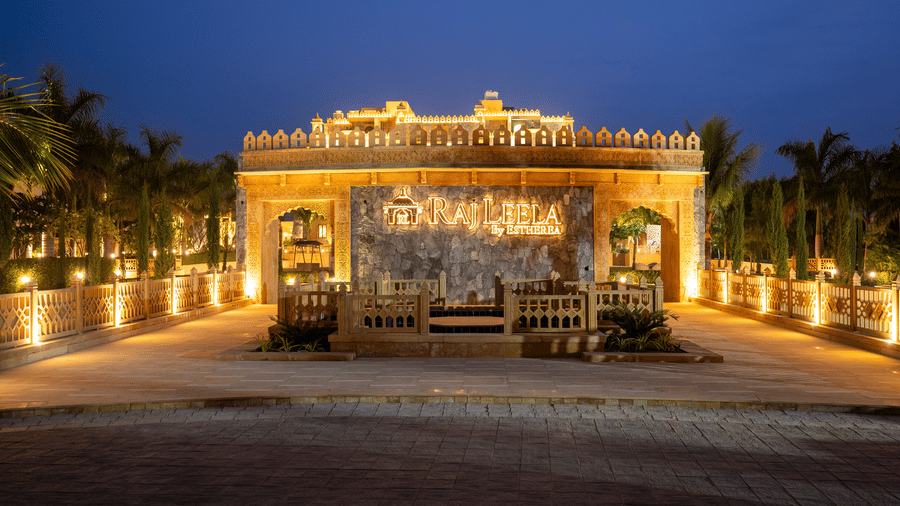 The grand entrance gate of EsthereaRaj Leela, Ranakpur lit up at night, featuring traditional stone carvings and a paved driveway.