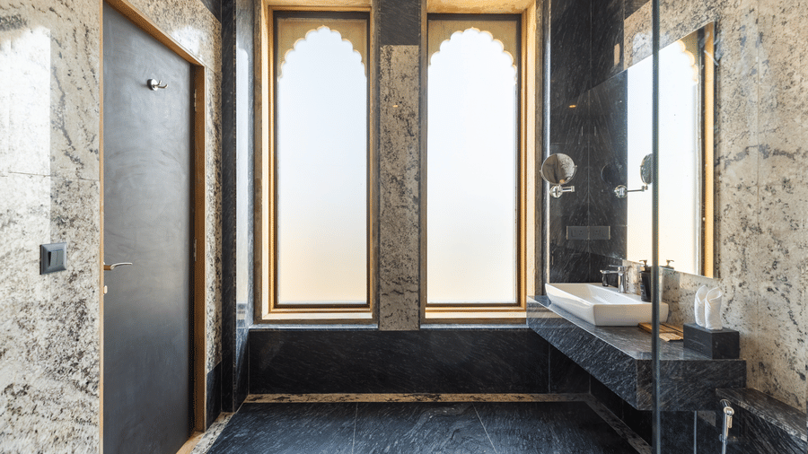 Bathroom featuring black and white marble surfaces, a vessel sink, and tall arched windows at EsthereaRaj Leela, Ranakpur.