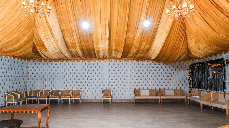 An indoor banquet hall in Jaipur at Estherea Resort & Spa featuring a draped gold fabric ceiling, chandeliers, and rows of chairs.