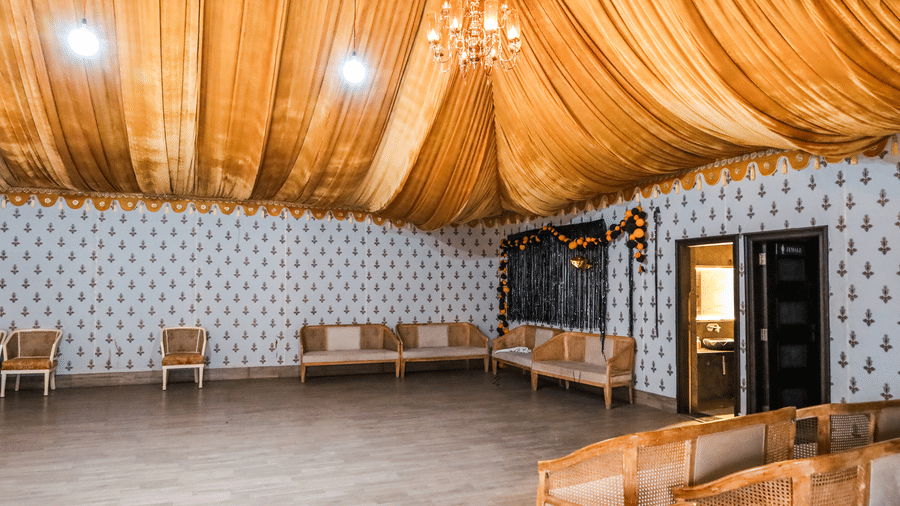 Indoor banquet hall at Estherea Resort & Spa, Jaipur, with patterned walls, wooden flooring, draped ceiling, a chandelier, and cushioned bench seating.