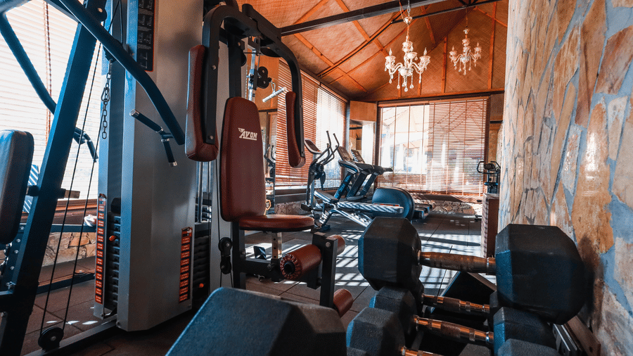 A wide view of the gym at Estherea Resort & Spa, Jaipur, equipped with stationary bikes, multi-gym weight systems, and large mirrors for workouts.