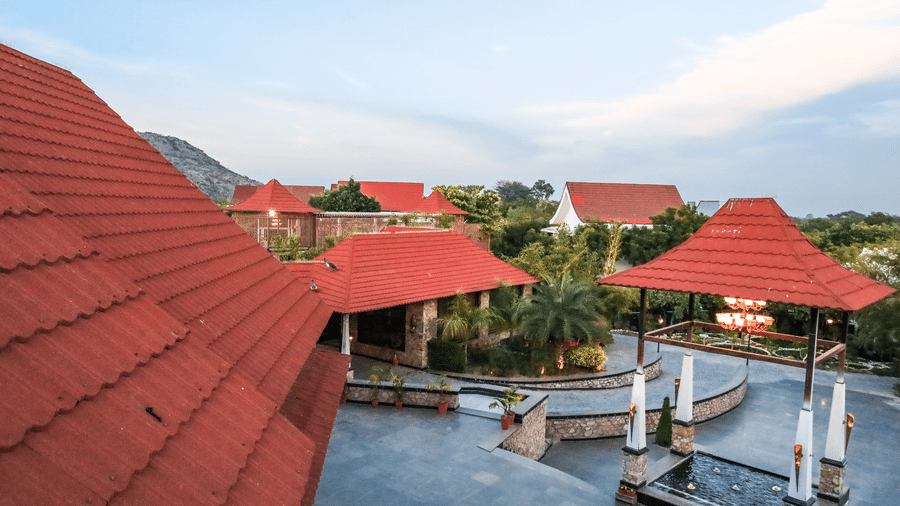 High-angle view of red-tiled roofs and a courtyard at Estherea Resort & Spa, Jaipur, featuring a fountain and white pillars in a circular drive.