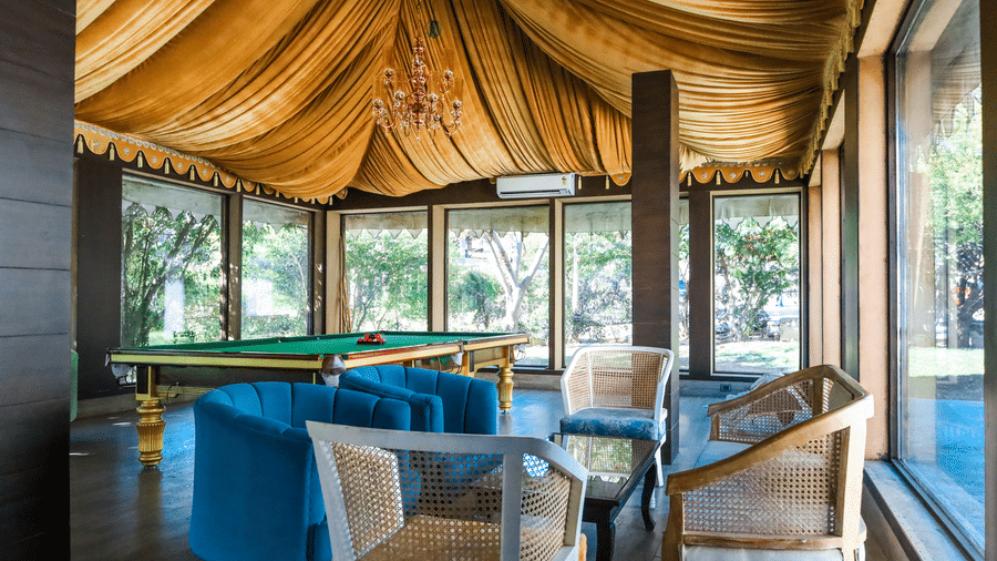 An indoor lounge in the games room at Estherea Resort & Spa, Jaipur with velvet armchairs, a coffee table, and a pool table visible in the background.