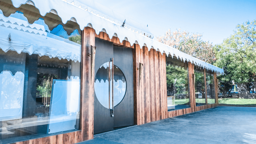 The modern wooden exterior of the indoor games room at Estherea Resort & Spa, Jaipur, featuring large glass windows and circular door handles.