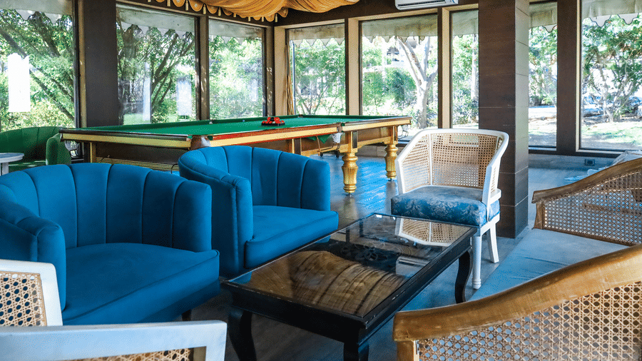 An indoor lounge in the games room at Estherea Resort & Spa, Jaipur with velvet armchairs, a coffee table, and a pool table visible in the background.