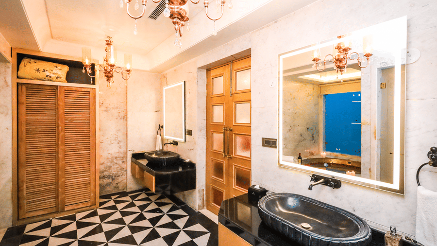 Bathroom at Estherea Resort & Spa, Jaipur with patterned black and white floor tiles, a stone sink, and a large illuminated mirror.