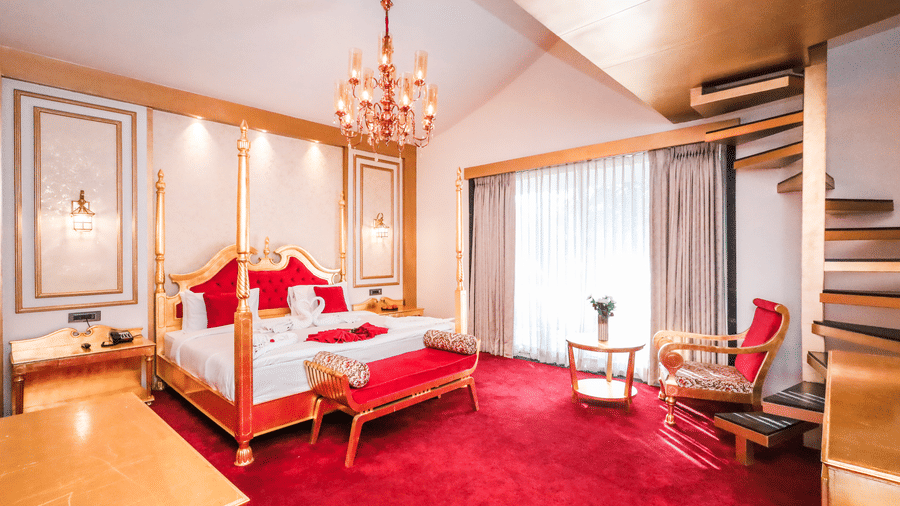Luxurious suite at Estherea Resort & Spa, Jaipur with red carpeting, a four-poster bed, and a wooden spiral staircase.