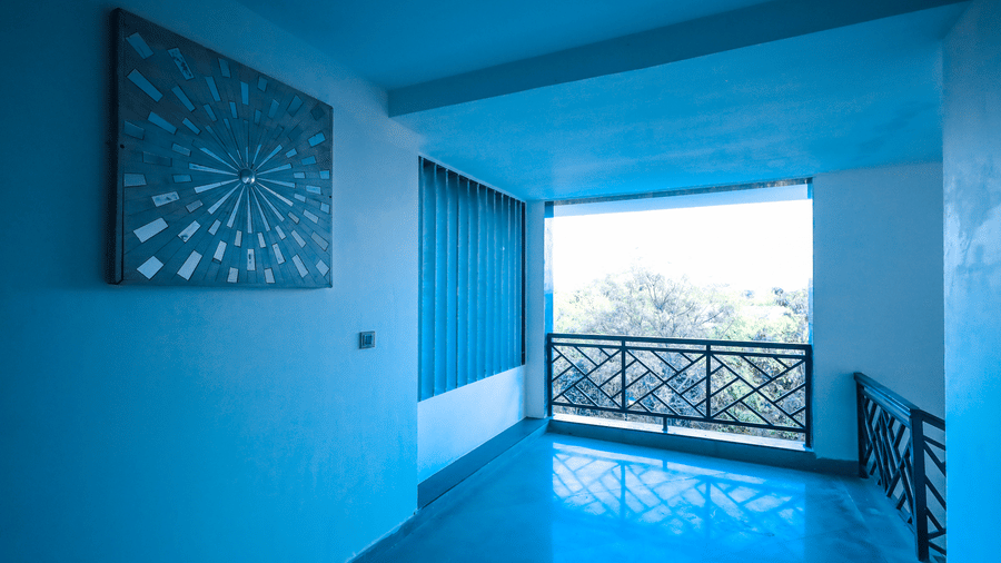 Interior hallway or balcony at Estherea Resort & Spa, Jaipur with blue-tinted walls, polished floors, and a black metal railing.