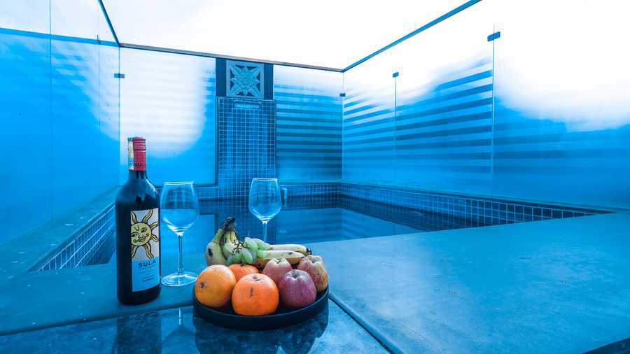 Close-up of a poolside setting at Estherea Resort & Spa, Jaipur featuring a bottle of wine, two glasses, and a platter of fresh fruit.