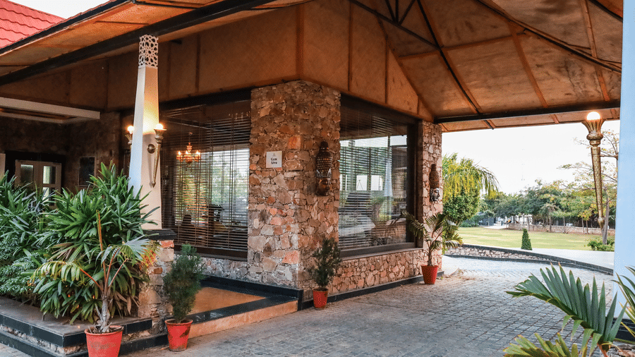 Exterior entrance of the Estherea Resort & Spa, Jaipur fitness centre, featuring stone-clad pillars, glass walls, and potted plants on the porch.