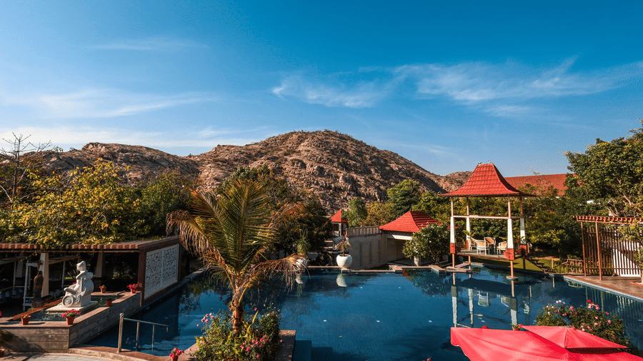 Panoramic view of the swimming pool and resort grounds at Estherea Resort & Spa, Jaipur, nestled between greenery and hills.