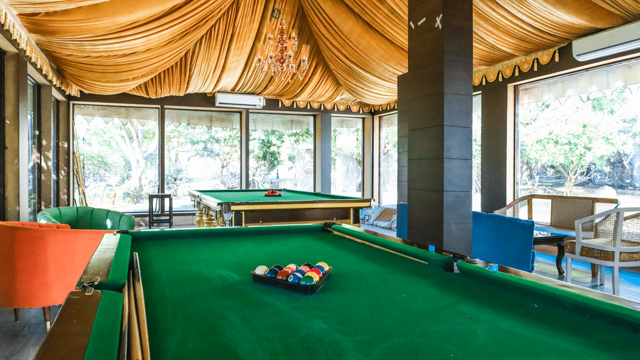 A recreation room at Estherea Resort & Spa, Jaipur featuring a green billiards table set under a draped fabric ceiling and large windows.