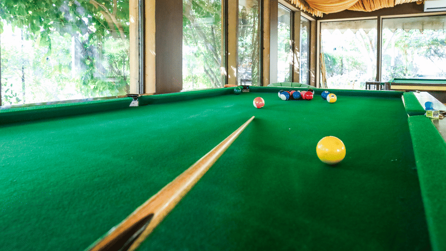 A recreation room at Estherea Resort & Spa, Jaipur featuring a green billiards table set under a draped fabric ceiling and large windows.