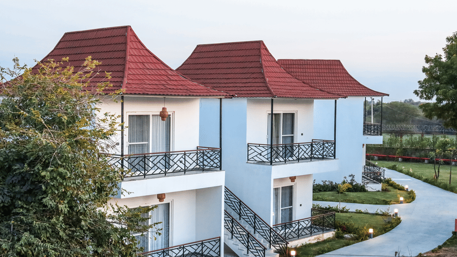 A row of white 2-storey villas at Estherea Resort & Spa, Jaipur with red pitched roofs, black metal balconies, and a paved walkway.