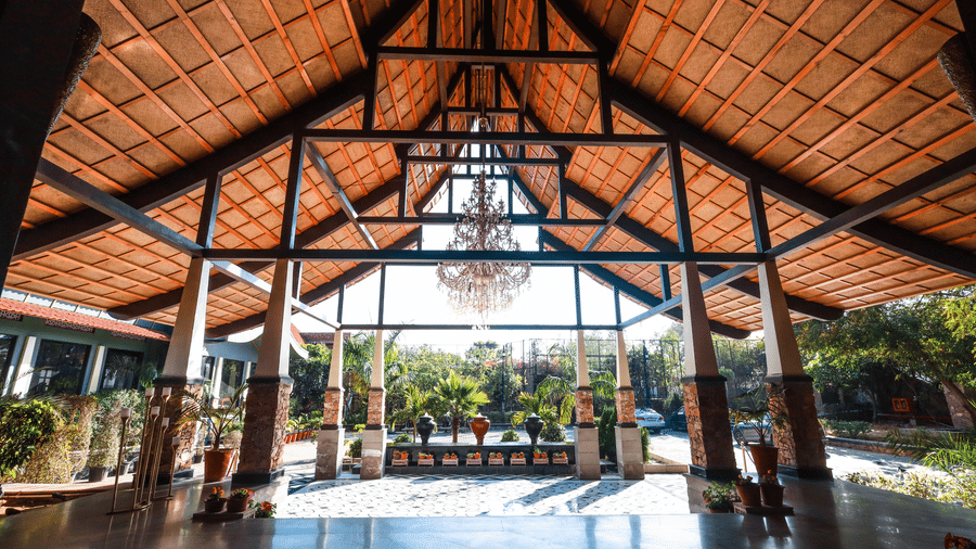 Wide view of the timber-framed pavilion at Estherea Resort & Spa, Jaipur, showing a symmetrical architectural design and hanging chandelier.