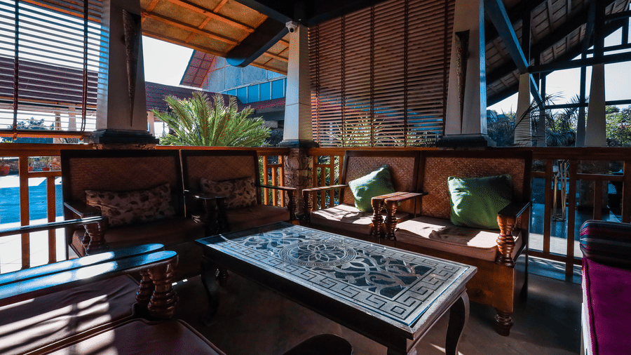 Shaded outdoor seating area at Estherea Resort & Spa, Jaipur, with dark wooden benches, green cushions, and a decorative stone-top table.
