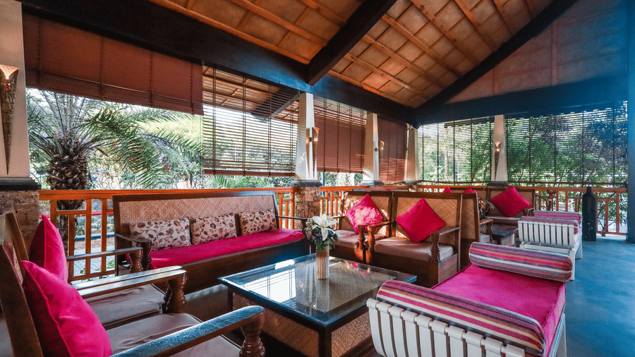 Group of wooden and white sofas with bright pink upholstery arranged in the open-air pavilion of Estherea Resort & Spa, Jaipur.