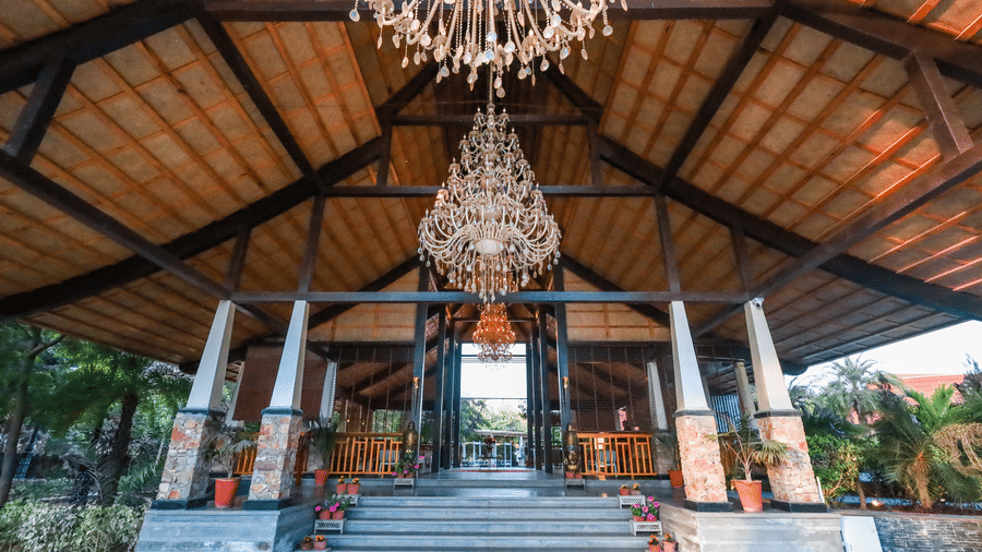 Low-angle view of the pavilion entrance at Estherea Resort & Spa, Jaipur, showcasing two large crystal chandeliers and a wide stone staircase.