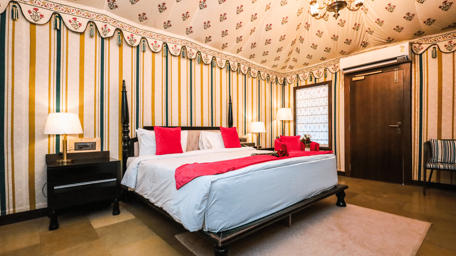 Bedroom at Estherea Resort & Spa, Jaipur featuring striped walls, a patterned ceiling, and a bed with red and white linens.