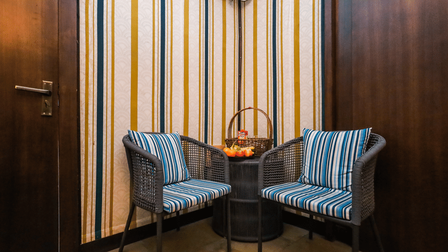 Indoor seating nook at Estherea Resort & Spa, Jaipur, featuring 2 striped armchairs and a small table against a striped wallpaper background.