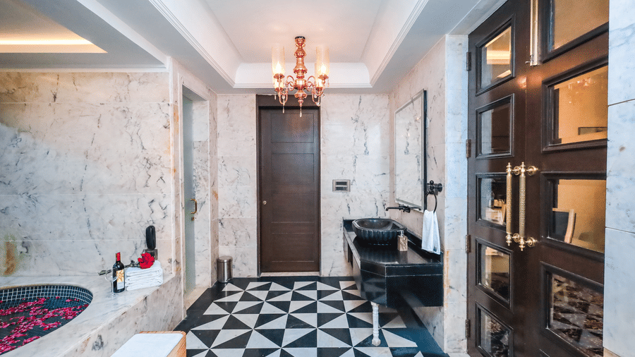 Interior view of a bathroom at Estherea Resort & Spa, Jaipur with a black marble vanity, geometric floor tiles, and a dark wooden door.