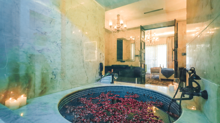 Close-up of a circular stone tub at Estherea Resort & Spa, Jaipur filled with red rose petals and surrounded by lit candles.
